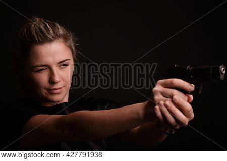 The Girl Narrowing Her Eyes, Aims To The Side From The Pistol, Which She Holds With Both Hands. The 