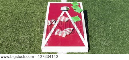 A Red And White Homemade Cornhole Game On A Green Turf Field With Green Bean Bags And Red And White 