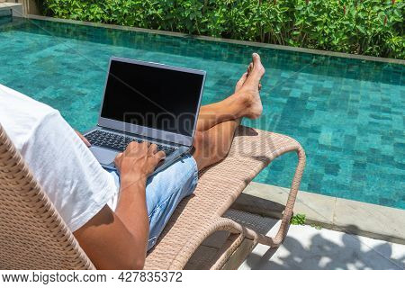 A Man Works Online With A Laptop By The Pool. Freelance, Work In Nature.