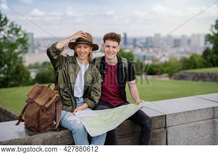 Young Couple Travelers With Map In City On Holiday, Resting And Looking At Camera.