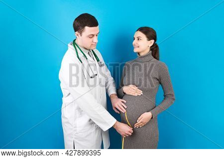 Happy Beautiful Pregnant Young Woman Touching Her Bare Tummy While A Doctor Is Measuring It