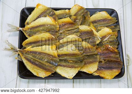Yellow Tabby (latin: Selaroides Leptolepis) Dried Folded In Rows On A Black Rectangular Plate With A