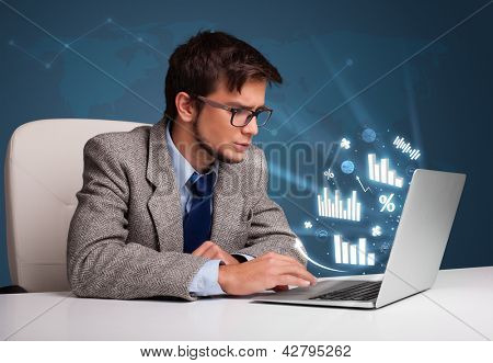 Joven sentado en el escritorio y escribiendo en el ordenador portátil con diagramas y gráficos que sale