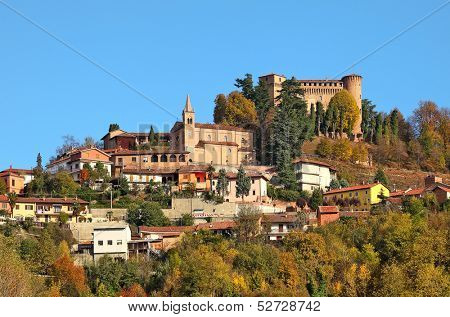 Small town and medieval castle among autumnal trees on top of the hill in Piedmont, Northern Italy.