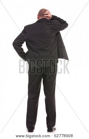 full length back view of a business man standing with a hand in his pocket and scratching his head with the other hand. on a white background