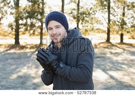 Portrait of a smiling young man in warm clothing shivering while having a walk in forest on a winter day