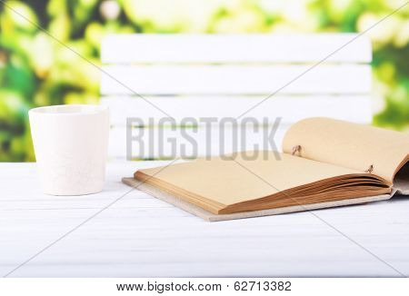 Empty notebook and cup of drink on wooden table, on bright background