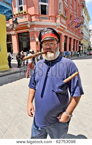 An old man standing on a street with a huge cigar