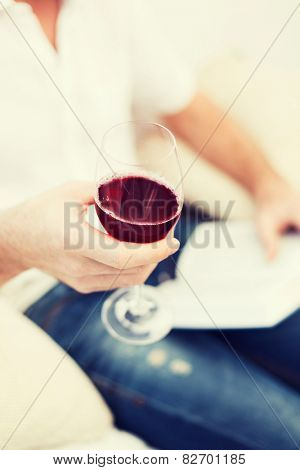 leisure, drinks, education and lifestyle concept - close up of male hand holdind book and glass of red wine