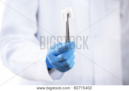 Doctor holding metal forceps with cheesecloth on white background