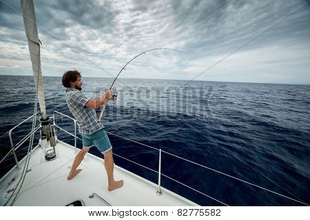 Young man fishing in open sea from sail boat