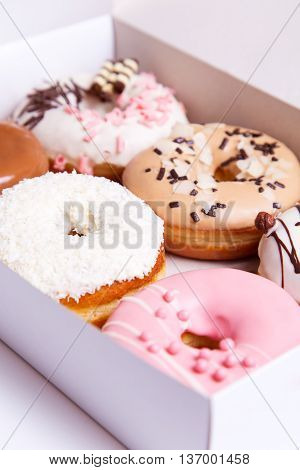 Colored donuts with sprinkles in a box on a white wooden background