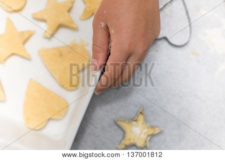 Homemade baking kitchen scene showing child holding baking tray with cut shortbread biscuits on baking paper ready to be cooked.
