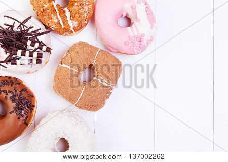 Colored delicious donuts with chocolate coconut and crispy sprinkles on a white wooden background