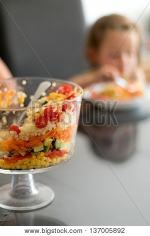 Multi Layered Salad in a Glass Trifle Bowl on on a glass table top with little girl in background narrow depth of focus.