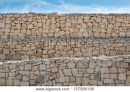 Limestone layered, rough dry stone wall, under a blue sky.