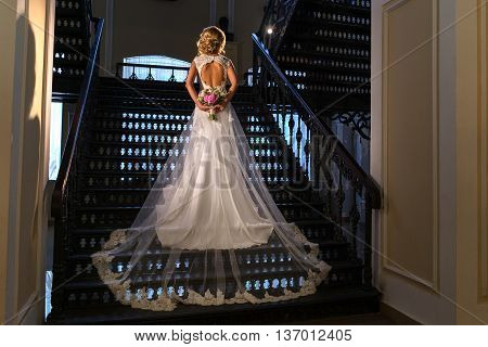 Bride in wedding luxury dress, back view. Stands on a beautiful cast-iron staircase.