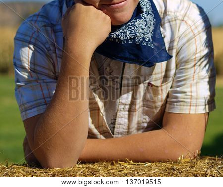 A young man poses on a hay bale with emphasis on his arms.