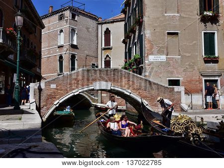 VENICE, ITALY - JUNE 18: A gondola with tourists pass under San Maria Nova medieval bridge JUNE 18, 2016 in Venice, Italy