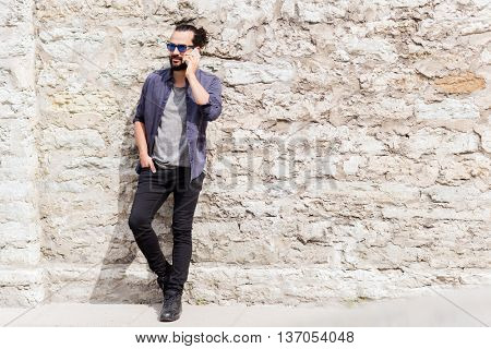 leisure, technology, communication and people concept - man calling on smartphone on street at stone wall