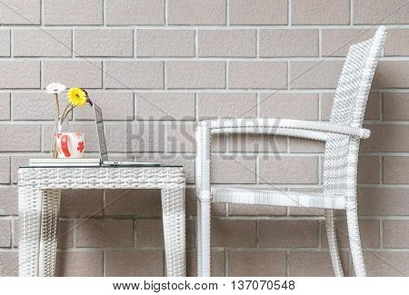 Closeup artificial colorful flower on glass bottle and computer on wood weave table with wood weave chair on blurred brown brick wall texture background beautiful interior in relaxation concept