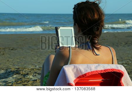 woman with brown hair reads the ebook on the beach