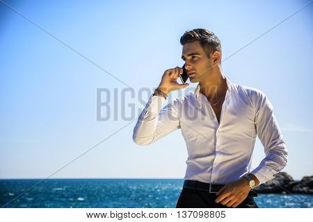 Young man at the seaside talking on cell phone while looking at the sea. Large copyspace