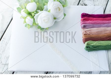 Materials for crosstitching on white wooden background selective focus rustic style