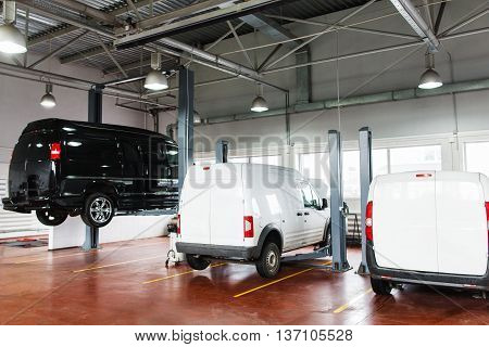 SUV big service station, black minibus raised up on lift. Front view on line of three cars in garage on service maintenance, two white pickups stay in stables, black minibus lifted up