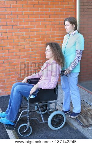 Nurse and patient in wheelchair in front of main entrance in medical facility, focus on nurse
