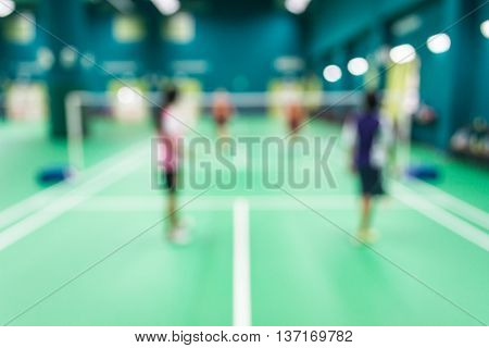 Blurred people playing badminton in green court.