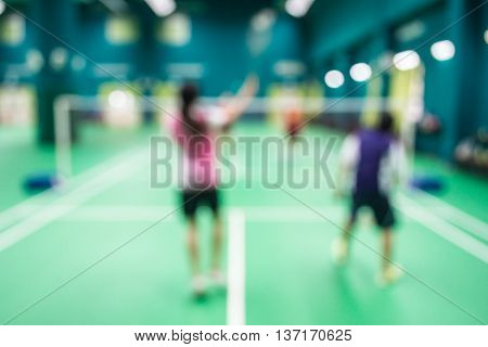 Blurred people playing badminton in green court.