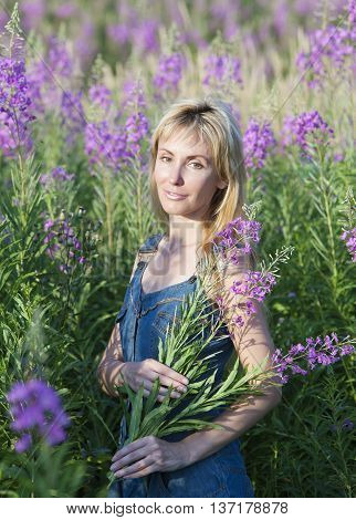 The smiling young woman with bunch of willowherb flower in the field