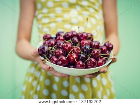 Girl on a background of turquoise wall holding a plate with cherry. Space for text