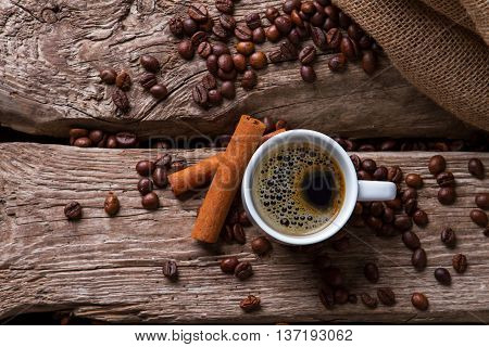 Cinnamon sticks and coffee cup. Roasted coffee beans near bag. Aromatic drink with specific taste. For lovers of espresso.