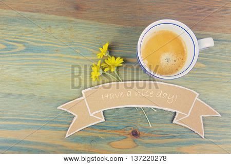 Coffee cup and daisy flowers with wish cardboard banner on wooden table. Have a nice day romantic concept. View from above
