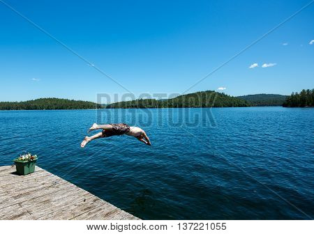 Man diving off a dock into a blue lake in the summer
