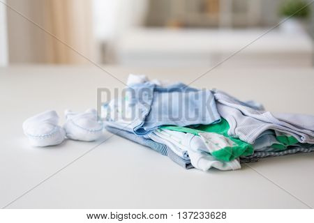 clothing, babyhood, motherhood and object concept - close up of baby bootees and pile of clothes for newborn boy at home