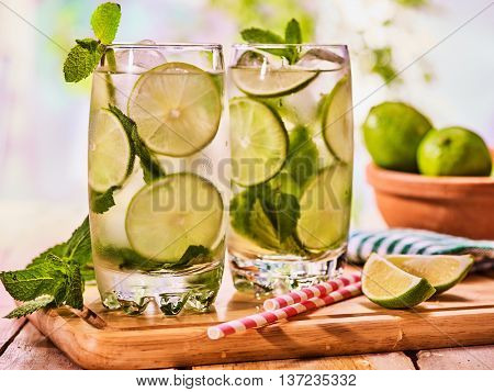 Alcohol drink. On wooden boards two glasses with alcohol drink and ice cubes. A drink number thirty three cocktail mohito with straw and lime and mint leaf. Country life. Outdoor. Light background.