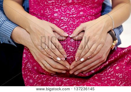Hands of men and women in the form of heart on a stomach of the pregnant woman