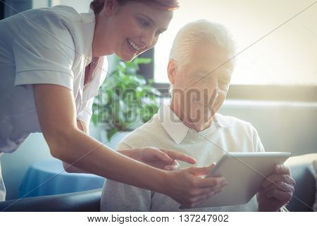 Female nurse showing medical report to senior man on digital tablet at home