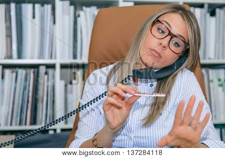 Close up of unmotivated blonde secretary polishing nails at workplace while talking on phone