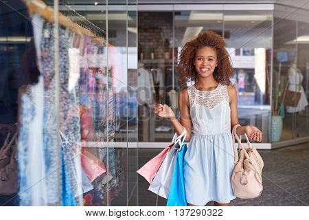 Attractive young woman with curly hair smiling and carrying shopping bags while enjoying a day shopping at the mall