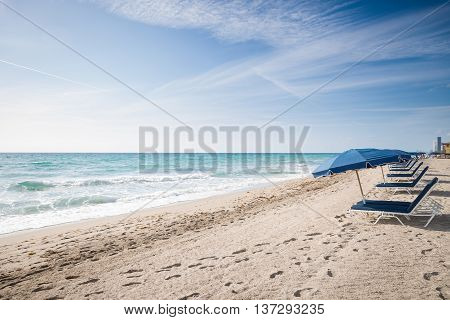 Beach in Miami FL. Open umbrellas on the sand beach at the ocean. Empty beach. Sea shore. Early morning. Clouds background.