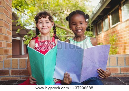 Two smiling children holding a book at school
