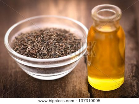 Caraway seeds with essential oil in glass bottle on wooden surface