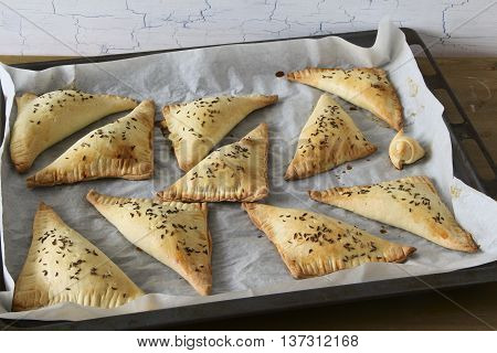 Homemade triangle pies on oven-tray and wooden background
