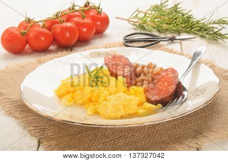 spanish breakfast with scrambled eggs on a plate chorizo baked beans fresh tomatoes rosemary and herbal scissor