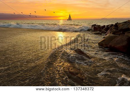 Sailboat sunset is a silhoueette of a sailboat with a white hot burning sun setting on the ocean horizon against a vivid orange sunset sky.