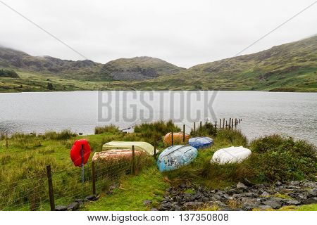 Old orange white and blue rowing boats by bank of Llyn Cwmystradllyn reservoir near Portmadog Gwynedd Wales UK.